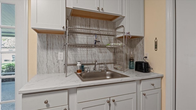 kitchen featuring backsplash, white cabinetry, sink, and light stone counters