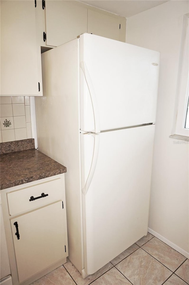 kitchen with light tile patterned floors, white cabinetry, white fridge, and tasteful backsplash