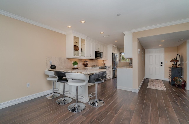 kitchen featuring white cabinetry, dark hardwood / wood-style floors, kitchen peninsula, a breakfast bar, and appliances with stainless steel finishes