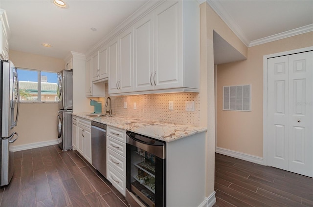 kitchen featuring beverage cooler, dark wood-type flooring, sink, stacked washer / dryer, and white cabinetry