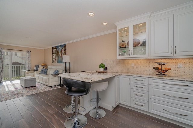 kitchen featuring a kitchen breakfast bar, dark hardwood / wood-style floors, light stone countertops, tasteful backsplash, and white cabinetry