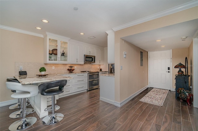 kitchen with a kitchen bar, dark wood-type flooring, white cabinets, and stainless steel appliances