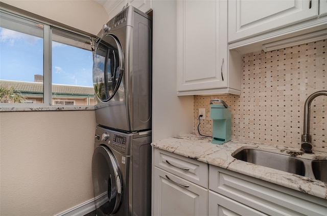 clothes washing area with cabinets, sink, and stacked washing maching and dryer