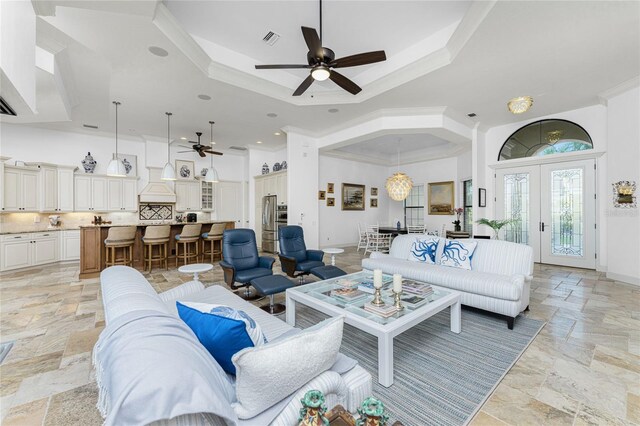 living room featuring ceiling fan with notable chandelier, a raised ceiling, ornamental molding, and french doors