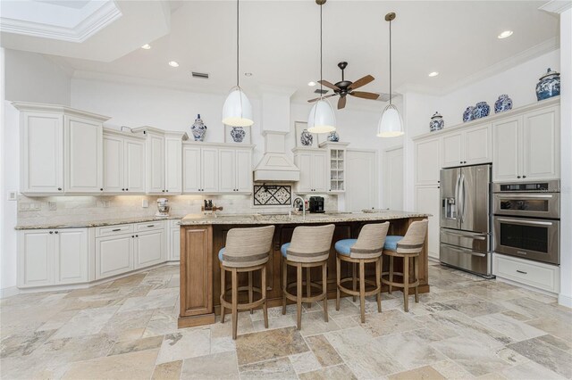 kitchen featuring backsplash, light stone counters, a kitchen island with sink, and appliances with stainless steel finishes