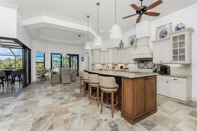 kitchen featuring white cabinetry, light stone countertops, a large island with sink, pendant lighting, and decorative backsplash