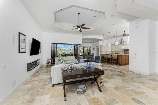 living room featuring a raised ceiling, ceiling fan, and ornamental molding