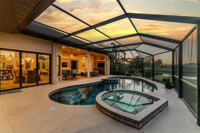 pool at dusk featuring a lanai, an in ground hot tub, and a patio