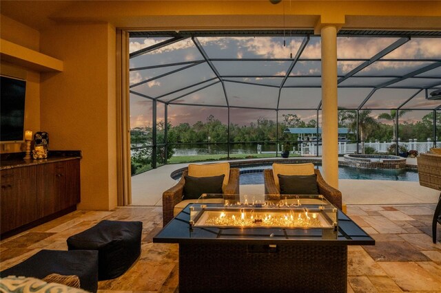 patio terrace at dusk featuring glass enclosure, an in ground hot tub, a water view, and a fire pit