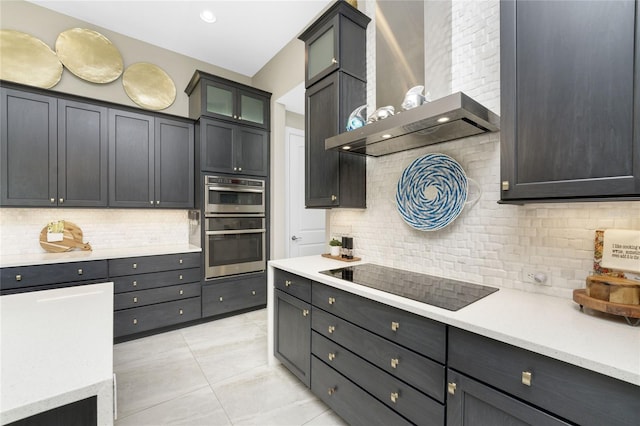 kitchen with black electric cooktop, wall chimney exhaust hood, light tile patterned floors, backsplash, and double oven