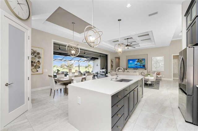 kitchen featuring sink, a kitchen island with sink, ceiling fan, pendant lighting, and stainless steel fridge