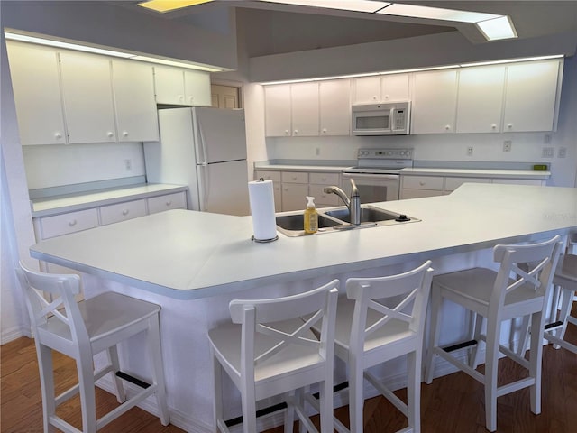 kitchen with dark wood-type flooring, white cabinets, sink, a kitchen breakfast bar, and white appliances