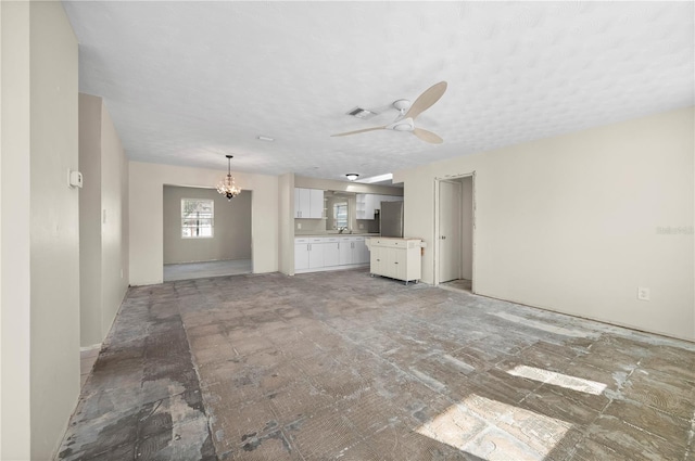 unfurnished living room with a textured ceiling and ceiling fan with notable chandelier