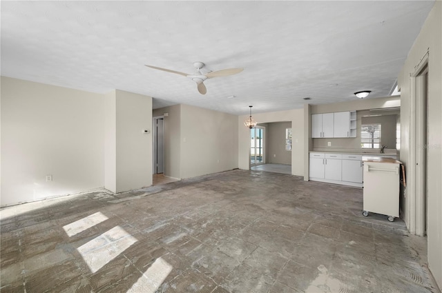 unfurnished living room featuring ceiling fan with notable chandelier and sink