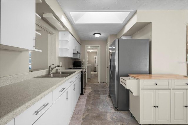 kitchen with wooden counters, appliances with stainless steel finishes, a skylight, sink, and white cabinets