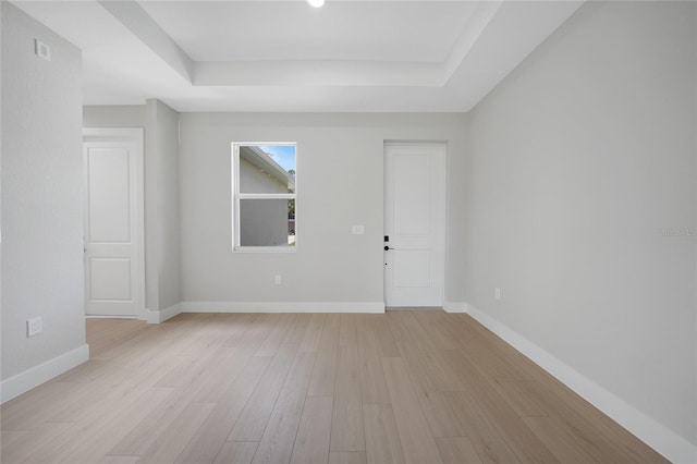 unfurnished room featuring a tray ceiling and light hardwood / wood-style flooring