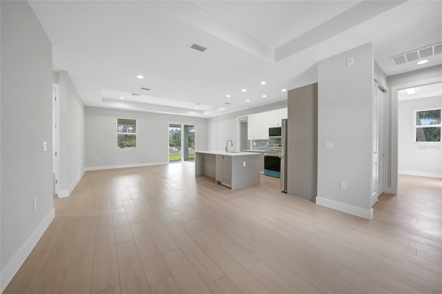 unfurnished living room featuring light wood-type flooring, a tray ceiling, and sink