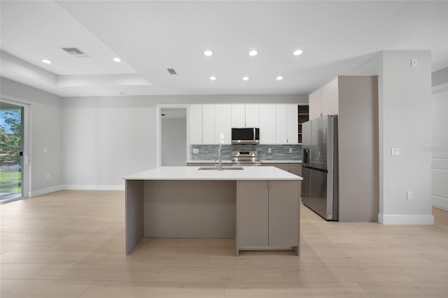 kitchen with tasteful backsplash, stainless steel appliances, white cabinetry, sink, and a kitchen island with sink