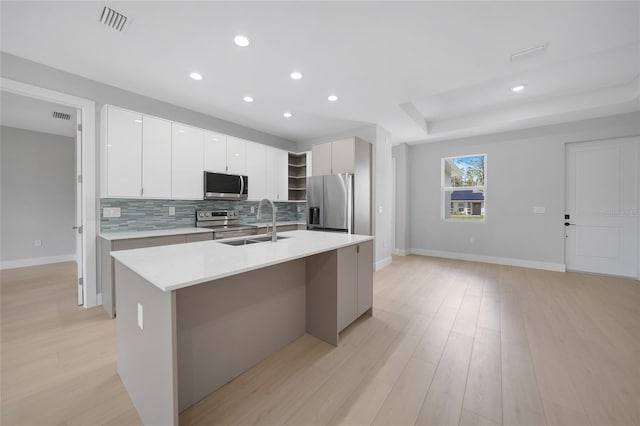 kitchen featuring white cabinetry, sink, appliances with stainless steel finishes, an island with sink, and light hardwood / wood-style flooring