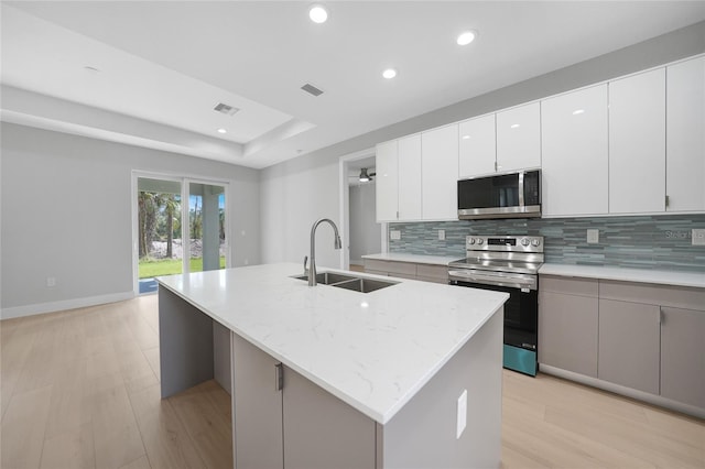 kitchen with a kitchen island with sink, appliances with stainless steel finishes, sink, and light hardwood / wood-style flooring