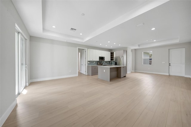 kitchen with appliances with stainless steel finishes, a kitchen island, a tray ceiling, and light hardwood / wood-style flooring