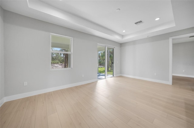 empty room featuring light wood-type flooring and a tray ceiling