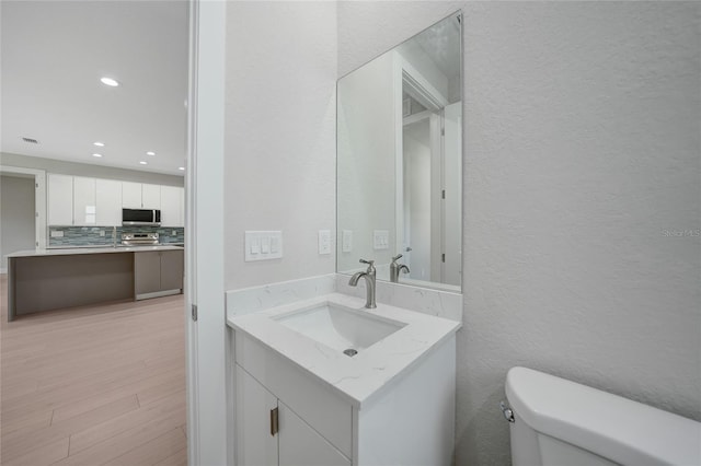 bathroom with toilet, tasteful backsplash, vanity, and hardwood / wood-style flooring