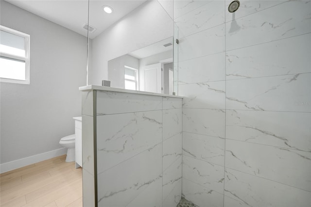 bathroom featuring toilet, wood-type flooring, and a tile shower