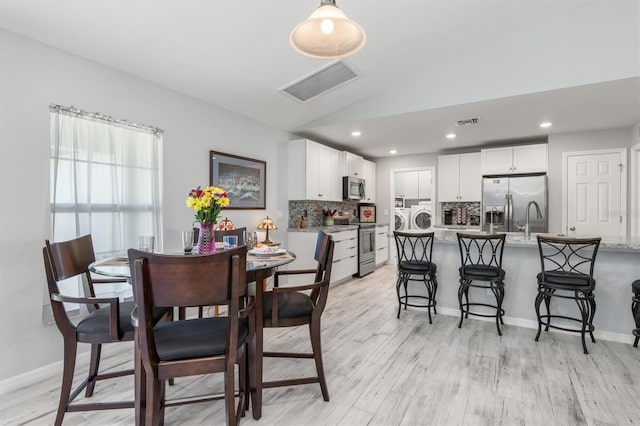 dining space with vaulted ceiling, washer and dryer, sink, and light hardwood / wood-style floors