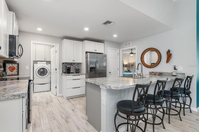 4340 Adolph Ave, North Port, FL 34288 - kitchen with appliances with stainless steel finishes, washer / dryer, a peninsula, light wood-style floors, and a breakfast bar