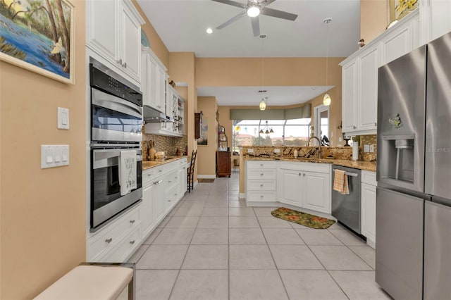 kitchen featuring stainless steel appliances, white cabinets, tasteful backsplash, light stone countertops, and decorative light fixtures