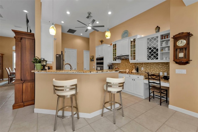 kitchen with a breakfast bar, kitchen peninsula, pendant lighting, light stone countertops, and white cabinets