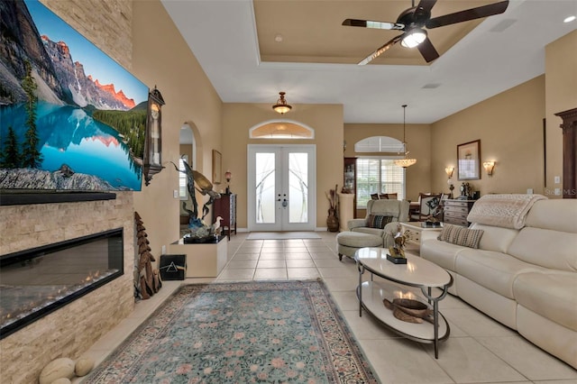 tiled living room with french doors, ceiling fan, a fireplace, and a tray ceiling