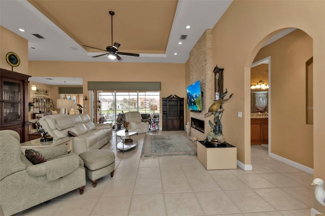 tiled living room with a fireplace, a raised ceiling, and ceiling fan