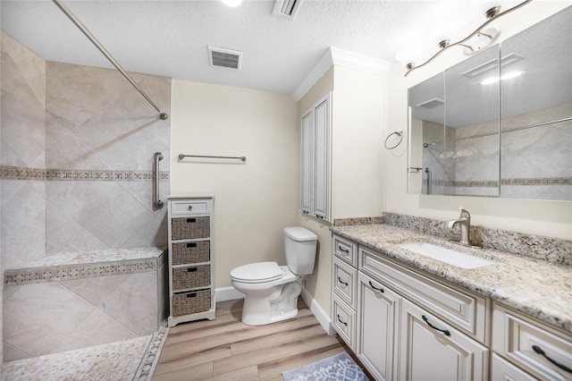 bathroom with hardwood / wood-style flooring, a textured ceiling, vanity, tiled shower, and toilet