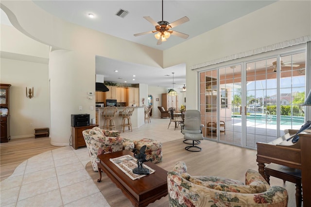 living room with a towering ceiling, light hardwood / wood-style floors, and ceiling fan