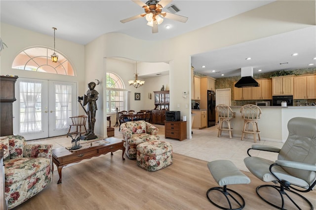 living room with light hardwood / wood-style floors, ceiling fan with notable chandelier, a towering ceiling, and french doors