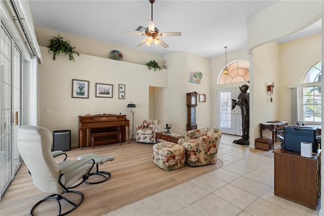 living room featuring a towering ceiling, light wood-type flooring, and ceiling fan