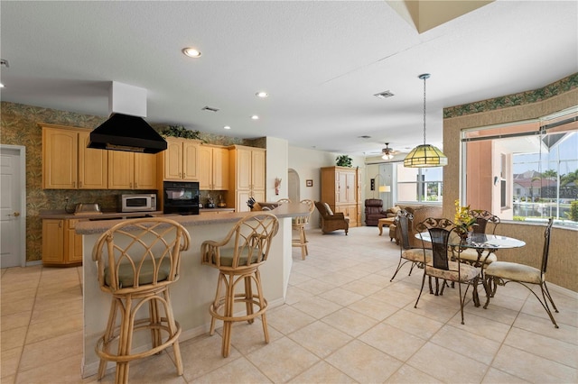 kitchen with island exhaust hood, a kitchen bar, hanging light fixtures, double oven, and ceiling fan