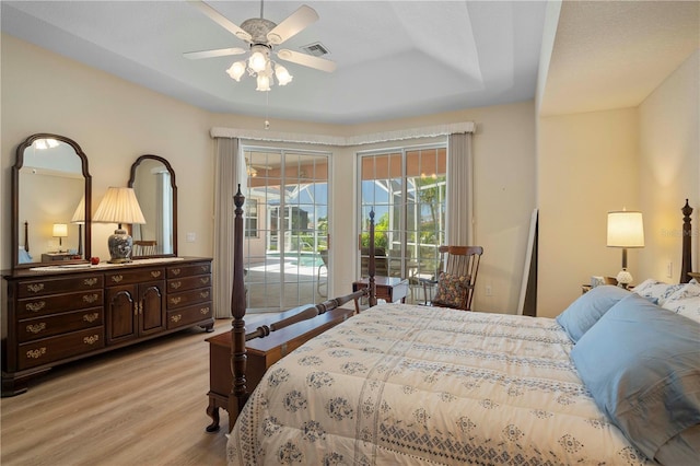 bedroom with access to exterior, light hardwood / wood-style flooring, ceiling fan, and a raised ceiling