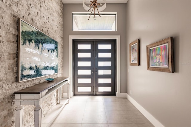 foyer entrance with a high ceiling, light tile patterned floors, an inviting chandelier, and french doors