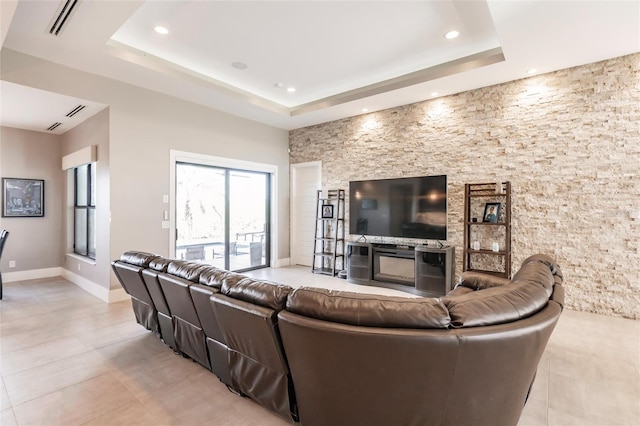 living room with a raised ceiling, a stone fireplace, and light tile patterned flooring