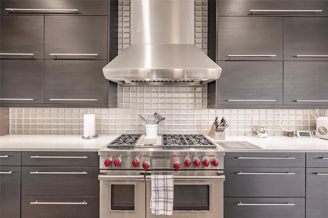 kitchen with gray cabinets, decorative backsplash, wall chimney exhaust hood, and double oven range