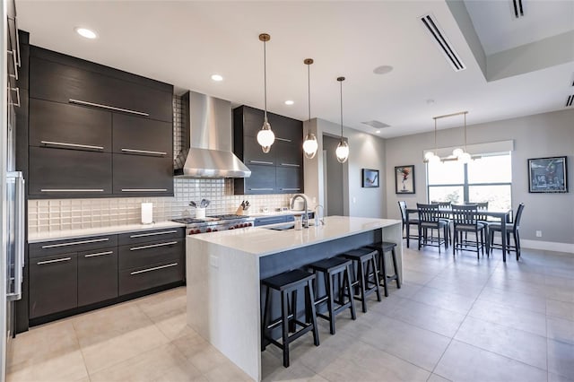 kitchen featuring a breakfast bar, sink, wall chimney range hood, hanging light fixtures, and an island with sink