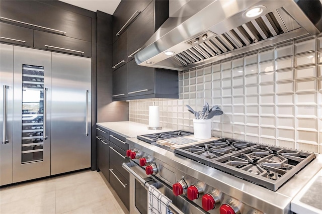 kitchen with decorative backsplash, premium appliances, wall chimney range hood, and light tile patterned floors