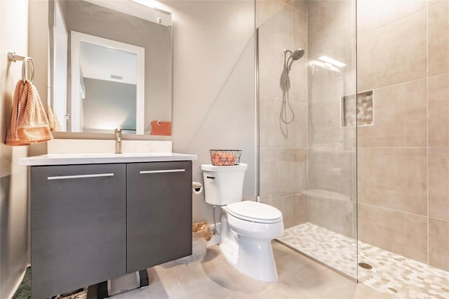 bathroom featuring tile patterned flooring, vanity, toilet, and a tile shower