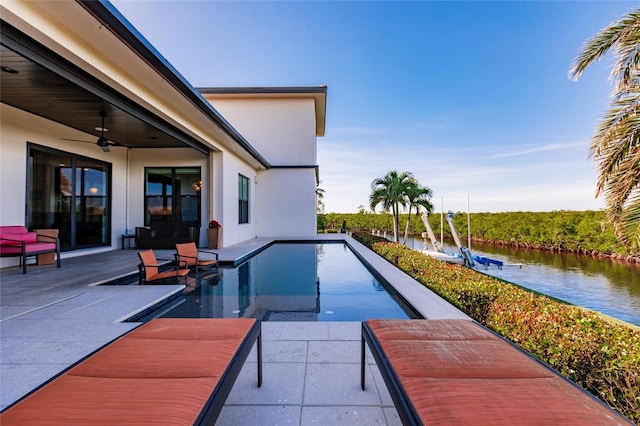 view of swimming pool featuring ceiling fan, a patio area, and a water view