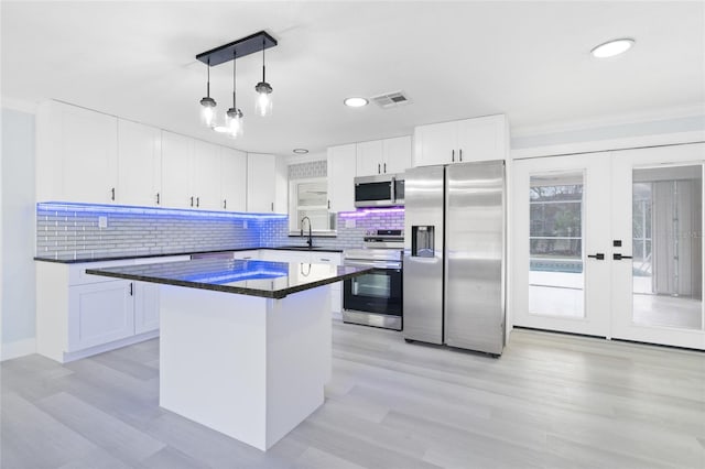 kitchen with appliances with stainless steel finishes, decorative light fixtures, sink, white cabinets, and a center island