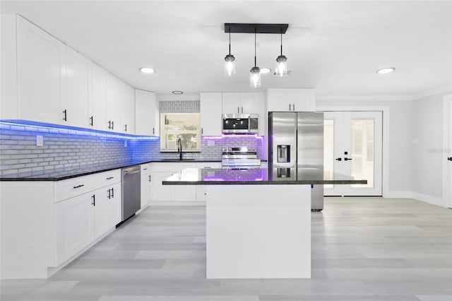 kitchen featuring stainless steel appliances, white cabinetry, backsplash, decorative light fixtures, and a center island