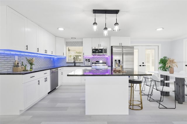 kitchen with a kitchen island, white cabinetry, appliances with stainless steel finishes, hanging light fixtures, and decorative backsplash